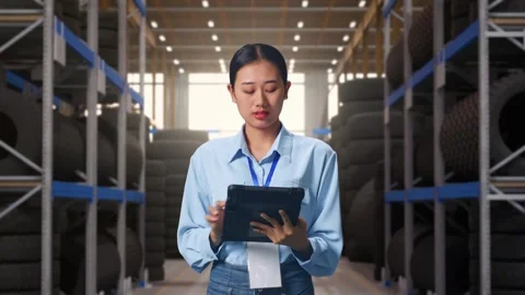 Asian Female Worker Working With A Tablet And Look Around at Tire Warehouse Stock Footage 341786019