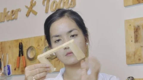 Asian female youth examines and glues wood model in a maker lab Stock Footage