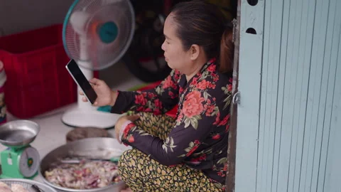 The Asian fishmonger combats boredom by checking her smartphone next to the fan Video stock 278374808