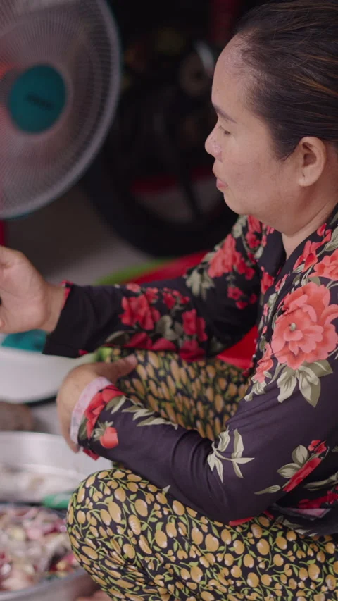 The Asian fishmonger combats boredom by checking her smartphone next to the fan Stock Footage 279423846