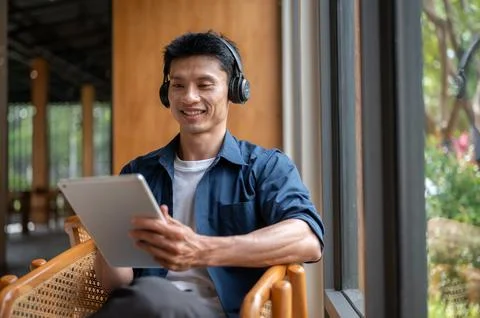 Asian freelancer man smiling while using a tablet and wearing headphones wo.. Stock Photos