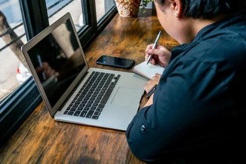 Asian freelancer writing notebook at rustic wooden table Stock Photos