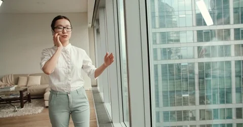Asian girl busy talking on the phone walks in a modern office, a beautiful view Stock Footage