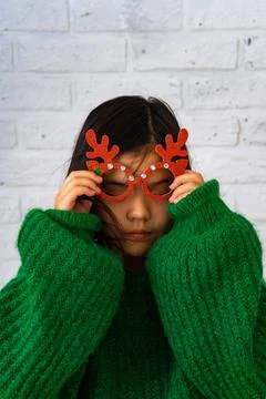 An Asian girl in a green sweater puts on masquerade glasses with deer horns Stock Photos