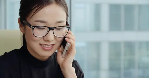 Asian girl with a smile talking on the phone in a modern office,Steadicam shot Stock Footage