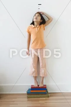 Asian girl standing on books in front of height markers Stock Photos