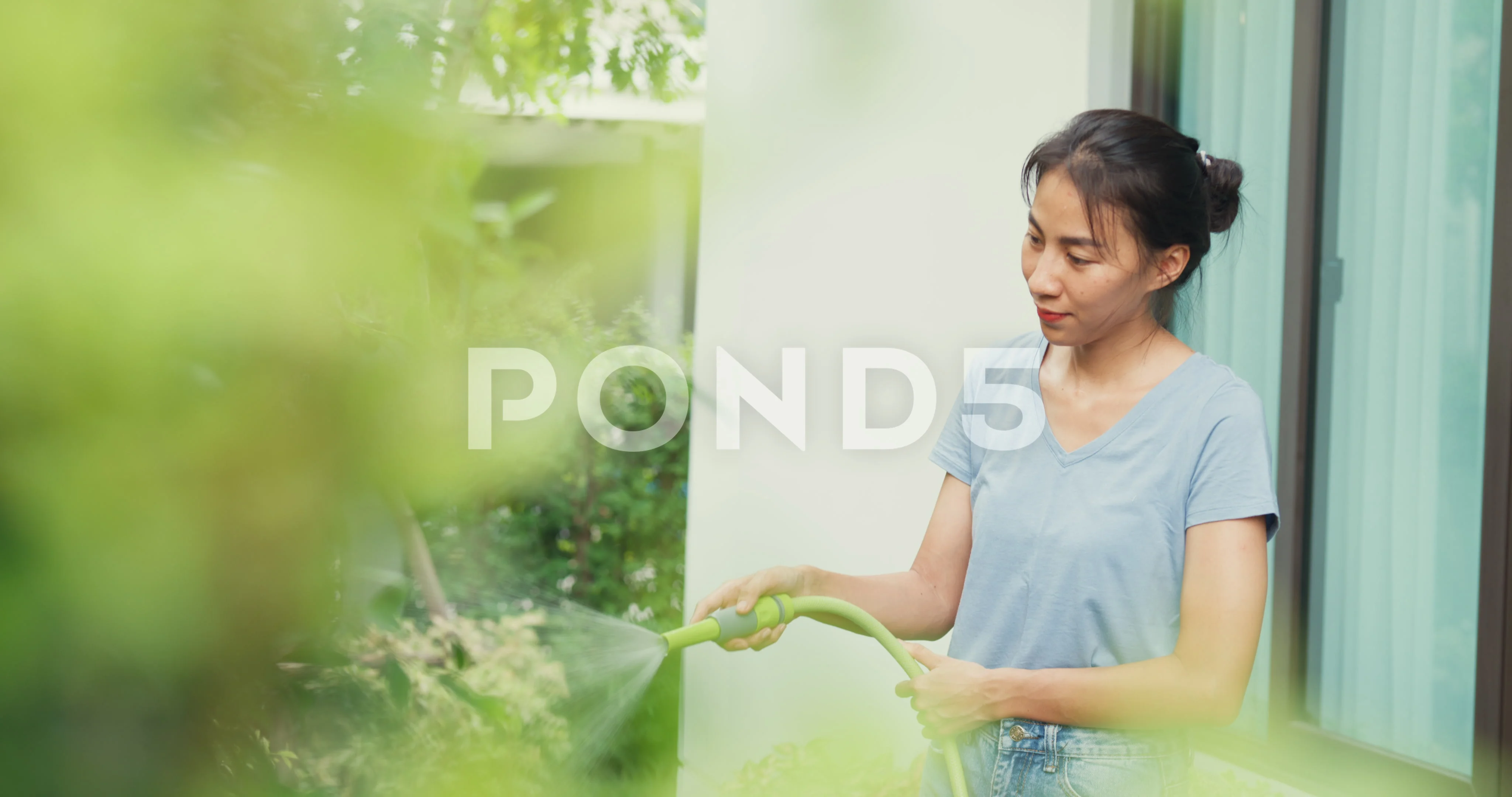 Close-up Cheerful happy Asian girl use garden hose watering plants