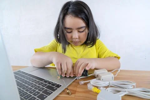An Asian girl using a laptop while assembling a robot from plastic bricks. ST Stock Photos