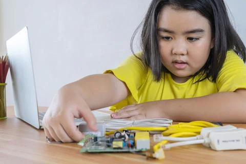 An Asian girl using a laptop while assembling a robot from plastic bricks. ST Stock Photos