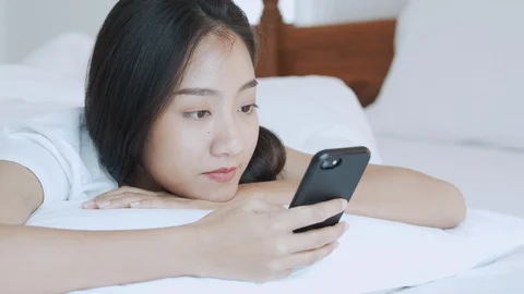 Asian girl is using  touchscreen smartphone using hand cover face for yawning Stock Footage 114309101
