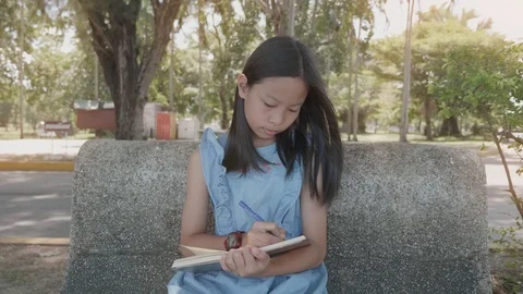 Asian girl writes in a notebook  sitting on a bench in the Park Stock Footage 118874953