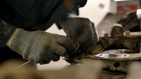 Asian in gloves and work clothes is repairing a spare part of a car in a garage Stock Footage 129834473