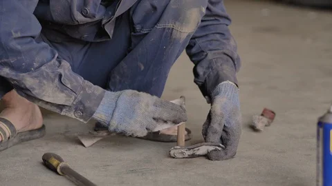 Asian in gloves and work clothes is repairing a spare part of a car in a garage Stock Footage 129840448