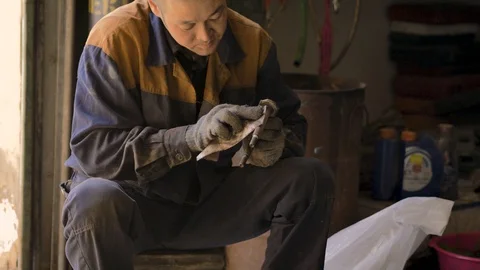 Asian in gloves and work clothes is repairing a spare part of a car in a garage Stock Footage 129842276