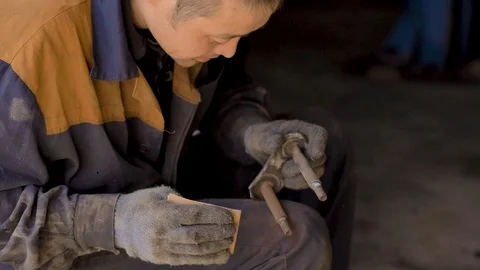Asian in gloves and work clothes is repairing a spare part of a car in a garage Stock Footage 129842456