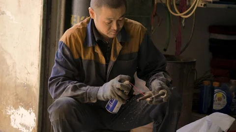 Asian in gloves and work clothes is repairing a spare part of a car in a garage Stock Footage 129842579