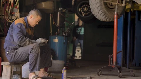Asian in gloves and work clothes is repairing a spare part of a car in a garage Stock Footage 129842775