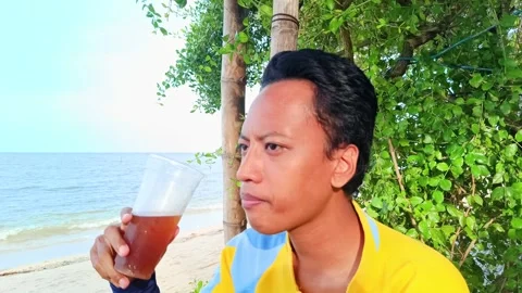 A asian guy is enjoying drinking iced tea with a beach Stock Footage 295477173
