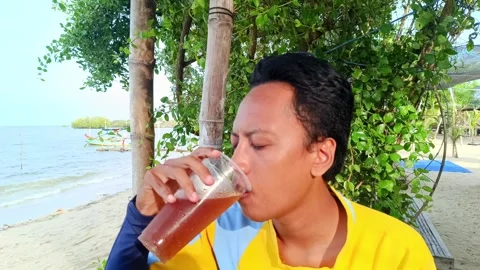 A asian guy is enjoying drinking iced tea with a beach Stock Footage 295477292