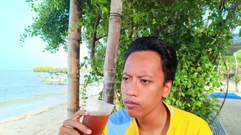 A asian guy is enjoying drinking iced tea with a beach Stock Footage 295477564
