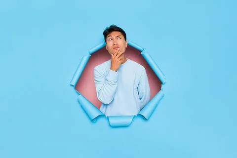 Asian guy posing in middle of blue background looking up at empty space Stock-Fotos