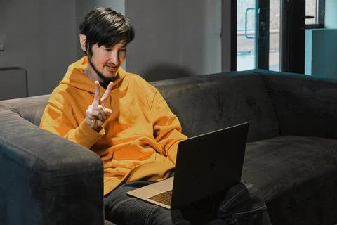 An Asian guy sits on sofa in a small office and communicates via laptop Foto stock