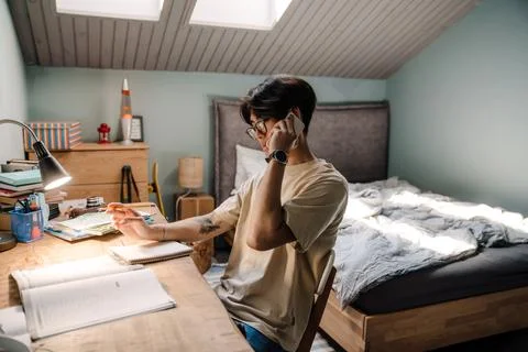 Asian guy using cellphone while sitting at desk and studying at home Stock Photos
