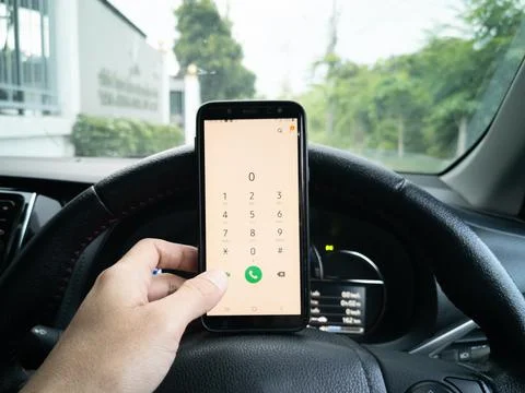 Asian hand, using smartphone on steering wheel (in car). Фото