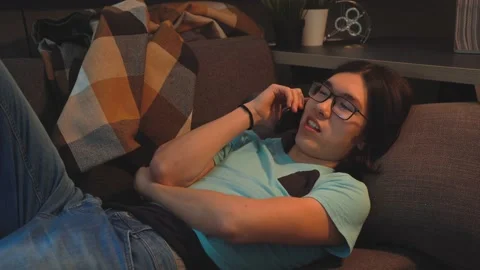 Asian Handsome  Man is Talking On Smart Phone At Home Laying on the Sofa Stock Footage 148347434