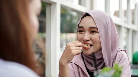 Asian hijab woman eat french fries in cafe with friend Stock Photos