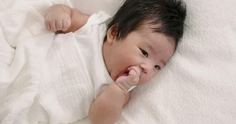 Asian infant boy lying on bed wrapped in white blanket sucking thumb with soft Stock Footage 326632519