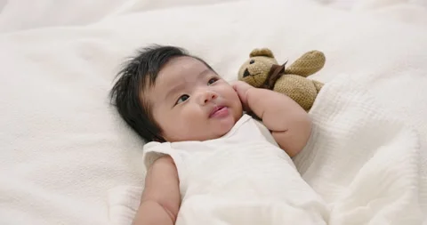 Asian infant boy lying on bed beside teddy bear looking upward with gentle 스톡 동영상 329951423