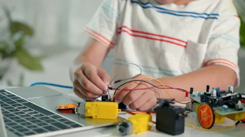 Asian kid boy plugging energy and signal cable to sensor chip with Arduino robot Stock Footage 200330573