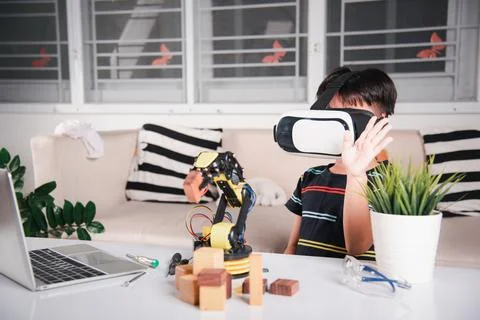 Asian kid boy using VR glasses on robotic arm in workshop Stock Photos