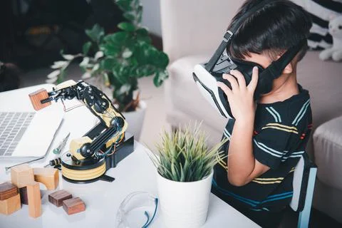 Asian kid boy using VR glasses on robotic arm in workshop Stock Photos