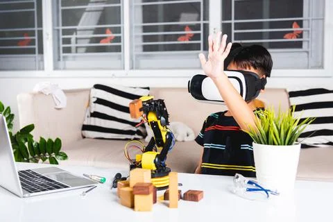 Asian kid boy using VR glasses on robotic arm in workshop Stock Photos