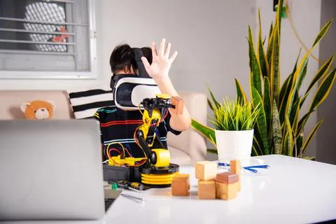 Asian kid boy using VR glasses on robotic arm in workshop Stock Photos