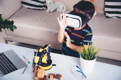 Asian kid boy using VR glasses on robotic arm in workshop Stock Photos