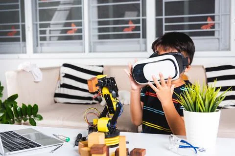 Asian kid boy using VR glasses on robotic arm in workshop Stockfoto's