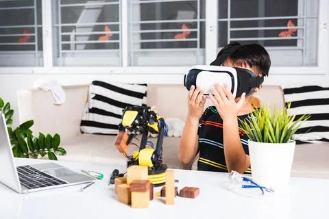 Asian kid boy using VR glasses on robotic arm in workshop Stockfoto's