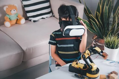 Asian kid boy using VR glasses on robotic arm in workshop Stock Photos