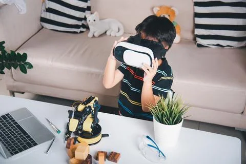 Asian kid boy using VR glasses on robotic arm in workshop Stock Photos