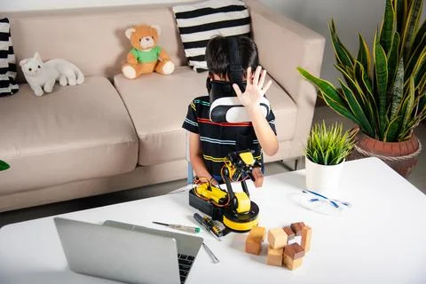 Asian kid boy using VR glasses on robotic arm in workshop Stock Photos