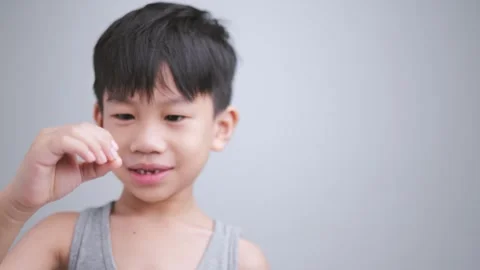 Asian kid holding the first fallen baby milk teeth while the second tooth loses. Video stock 247367504