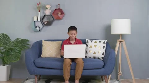 Asian kid sitting on couch using laptop notebook Stock Footage 155162314