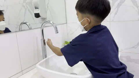 Asian kindergarten boy washes his hands with a faucet in restroom Stock Footage 258102416