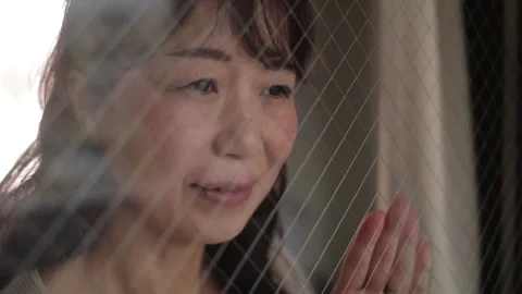 Asian lady looking outside through the window. Smile. Stock Footage 221084125