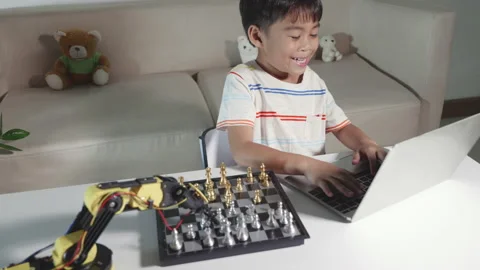 Asian little boy programming code to robot machine arm on laptop for play chess Stock Footage 194409547