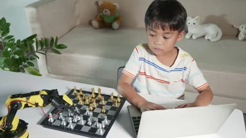 Asian little boy programming code to robot machine arm on laptop for play chess Stock Footage 201415875