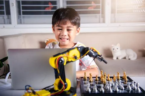 Asian little boy programming code to robot machine arm on laptop for play che Foto stock